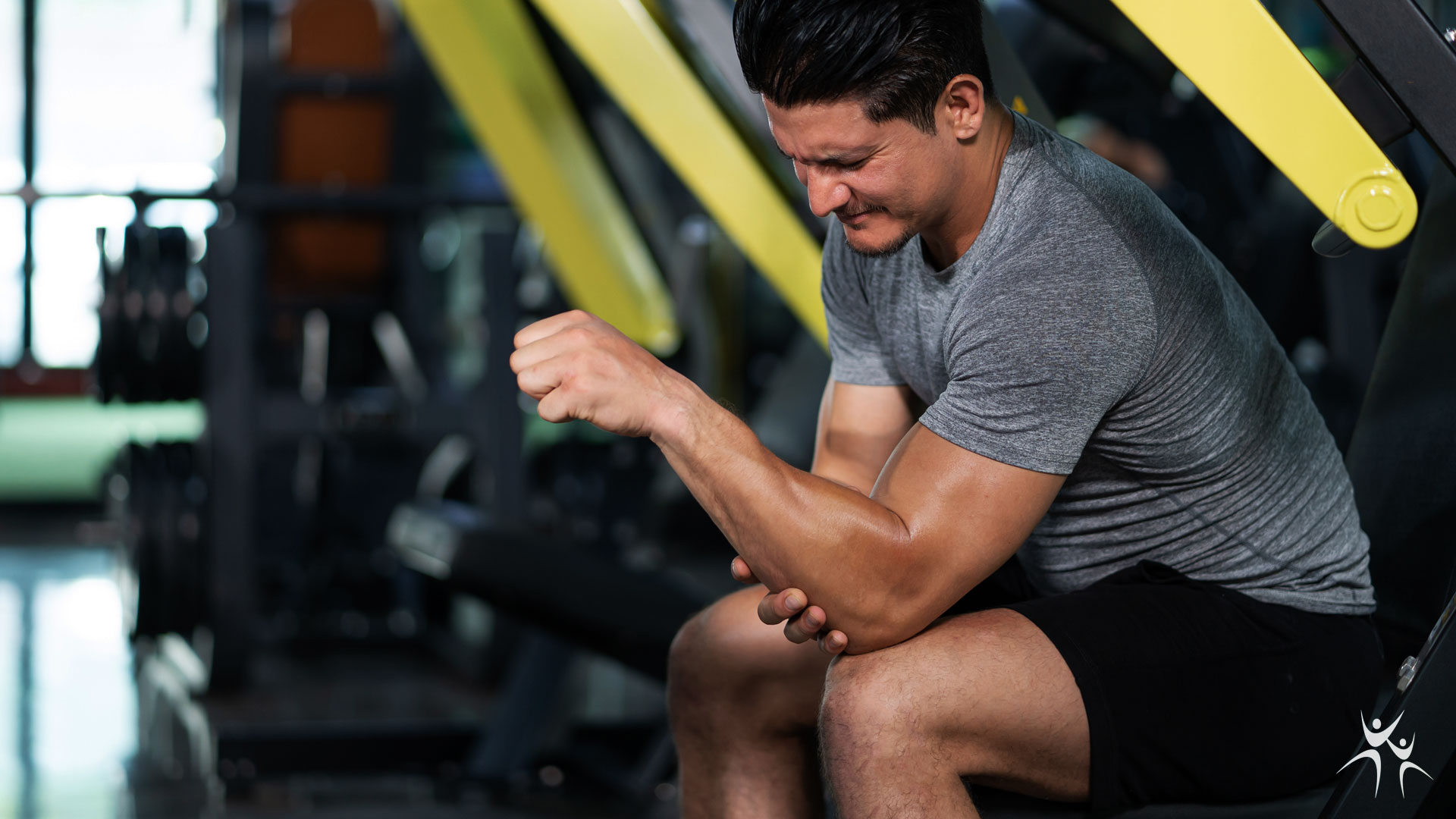 Man seated at gym clutching his elbow in pain