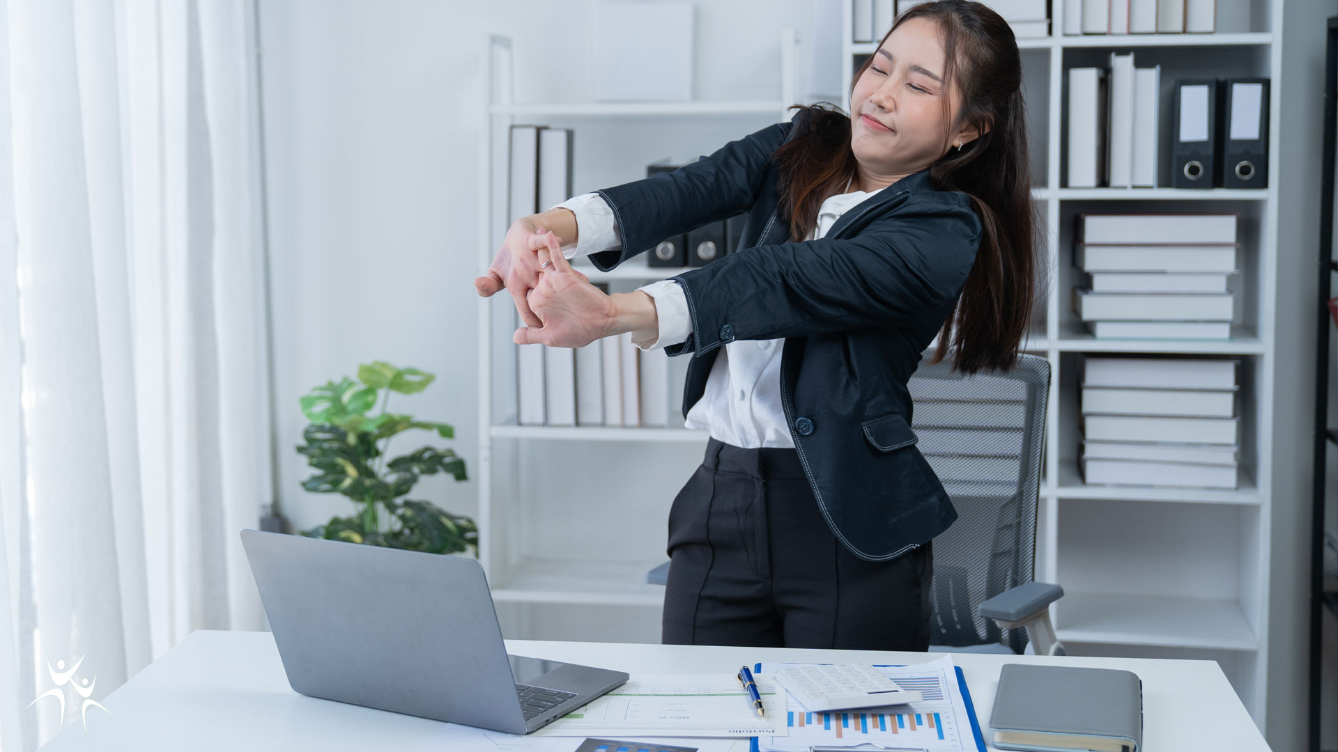 office worker standing at her desk stretching arms and back