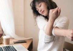 Office worker seated at desk stretching arms in front of her body