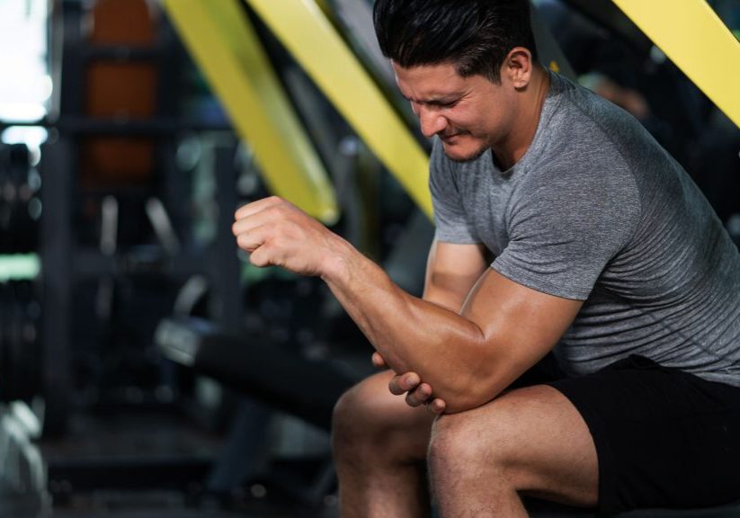 Man seated at gym clutching his elbow in pain