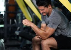 Man seated at gym clutching his elbow in pain