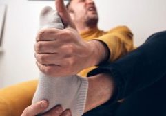 Man seated on couch and holding his foot in pain