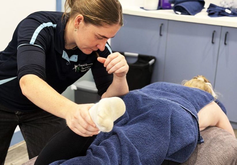 Osteo Meave Bohanna treating footy player's leg  as they lay on the treatment bed