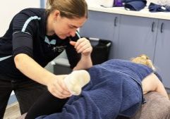 Osteo Meave Bohanna treating footy player's leg  as they lay on the treatment bed