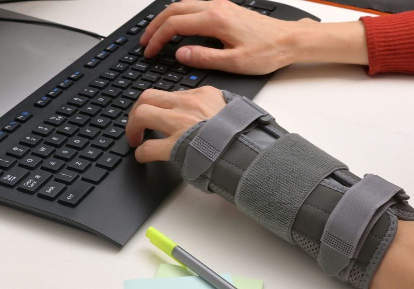 Closeup of person typing on a keyboard with one arm in a splint to support injury