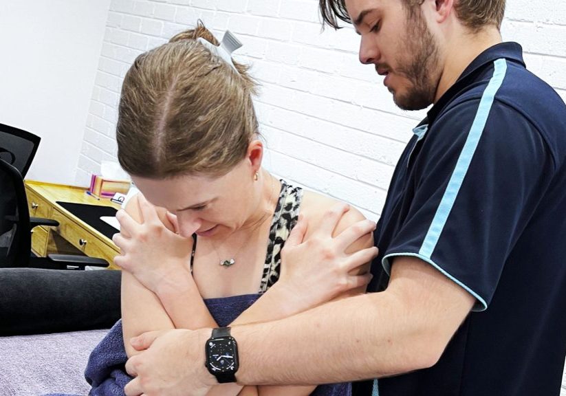 Dr Mitchell Pontefract examines seated client examining her spine