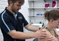 Osteopath Dr Mitchell examines a seated female patients back and shoulders